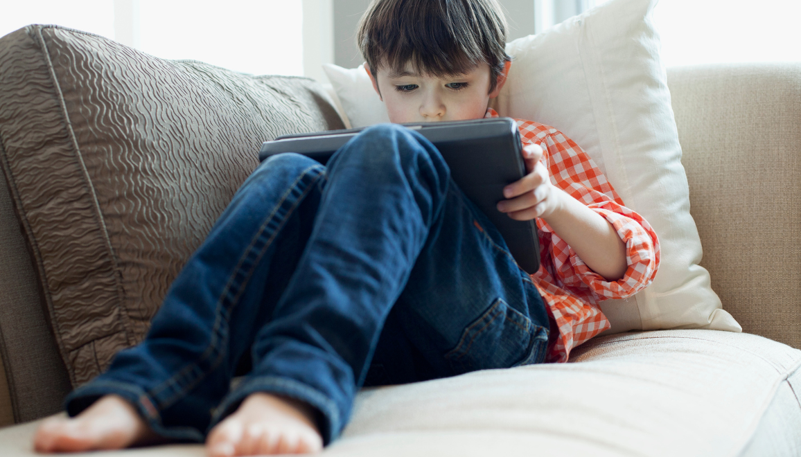 child sitting on a couch holding a tablet